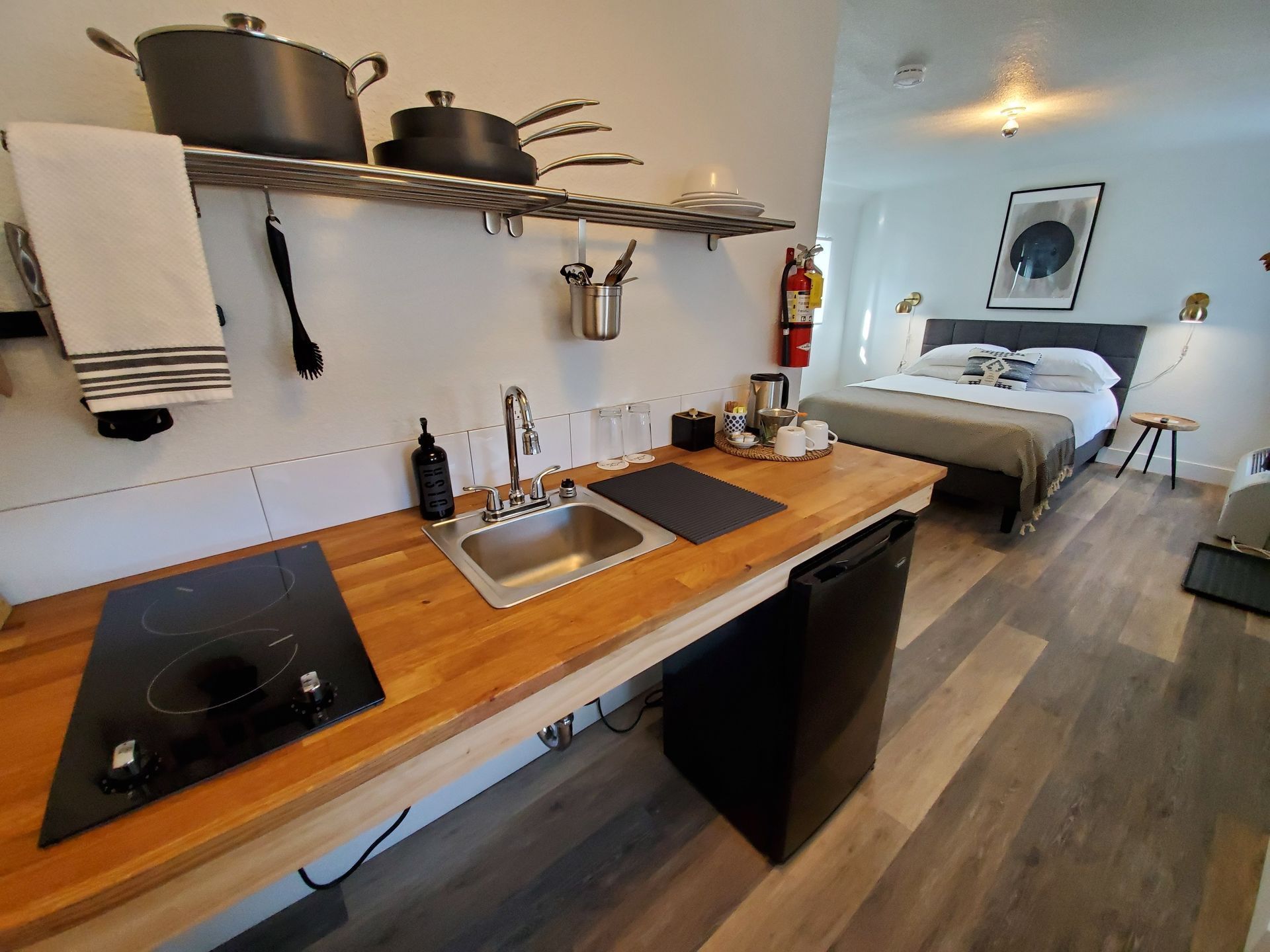 Small kitchen area with stovetop, sink, and storage, leading to a bedroom.