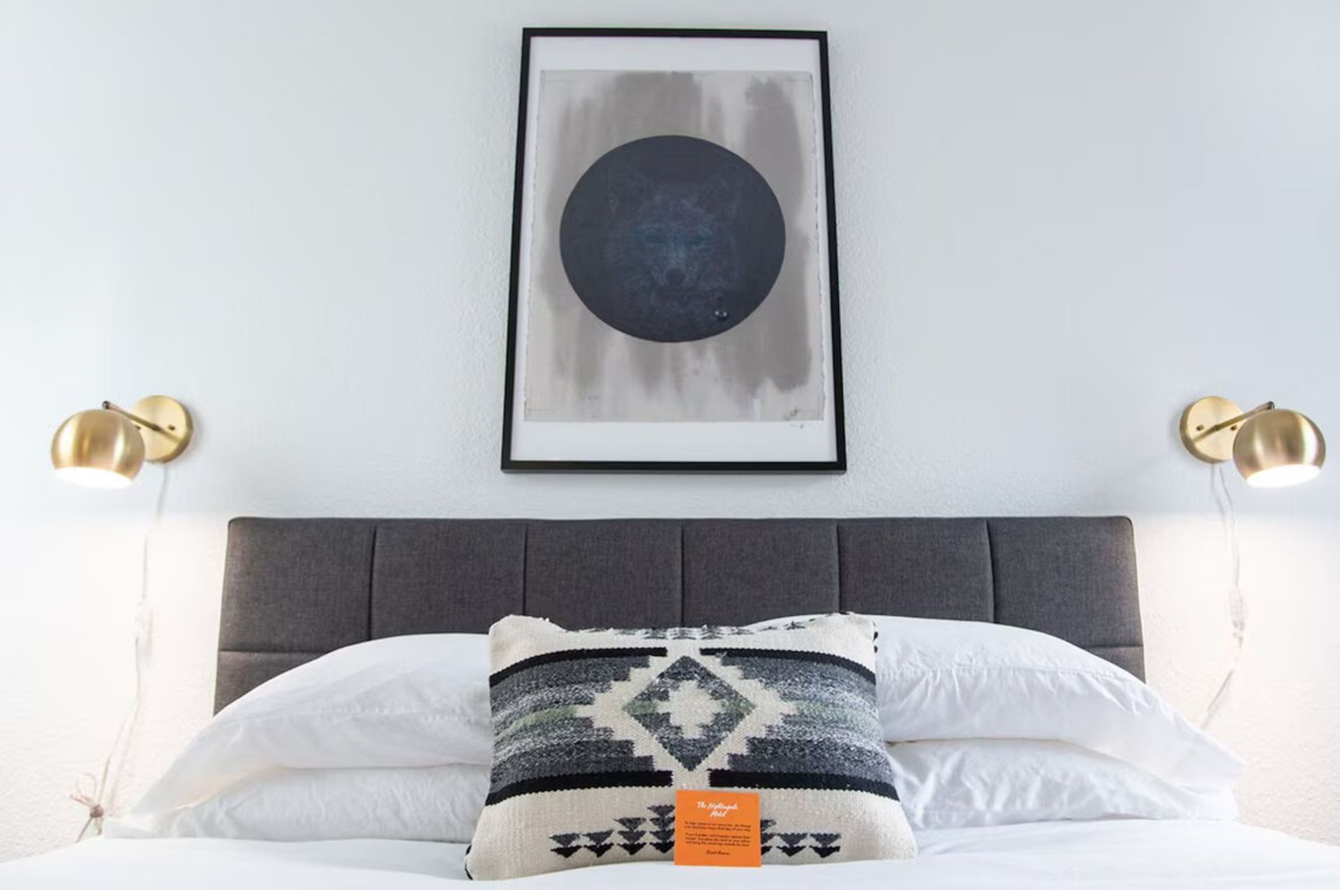 Bedroom with bed, gray headboard, and art print. Gold sconces on wall. Decorative pillow.
