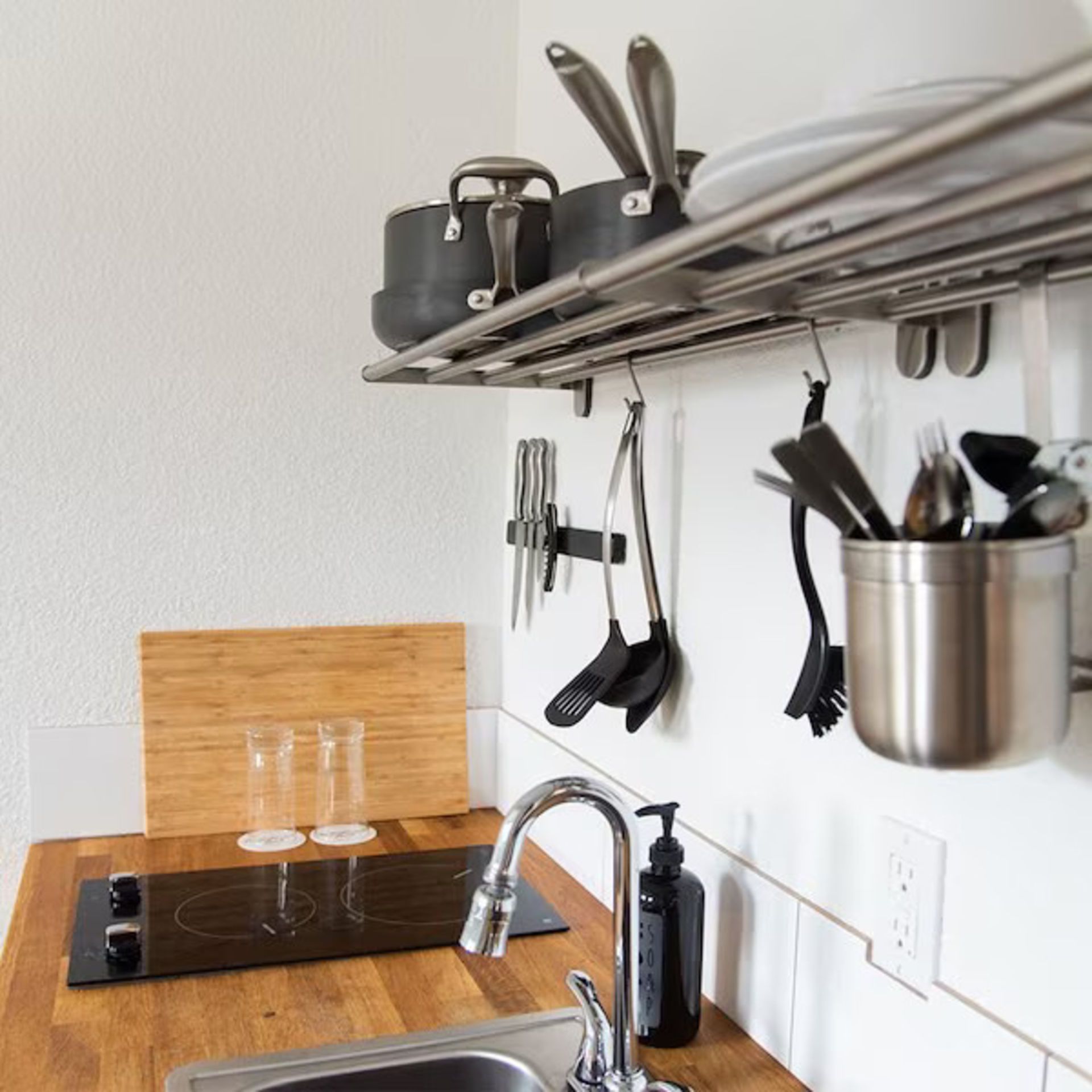 Small kitchen with stainless steel shelving holding pots, utensils, and dishware, with sink and stovetop.
