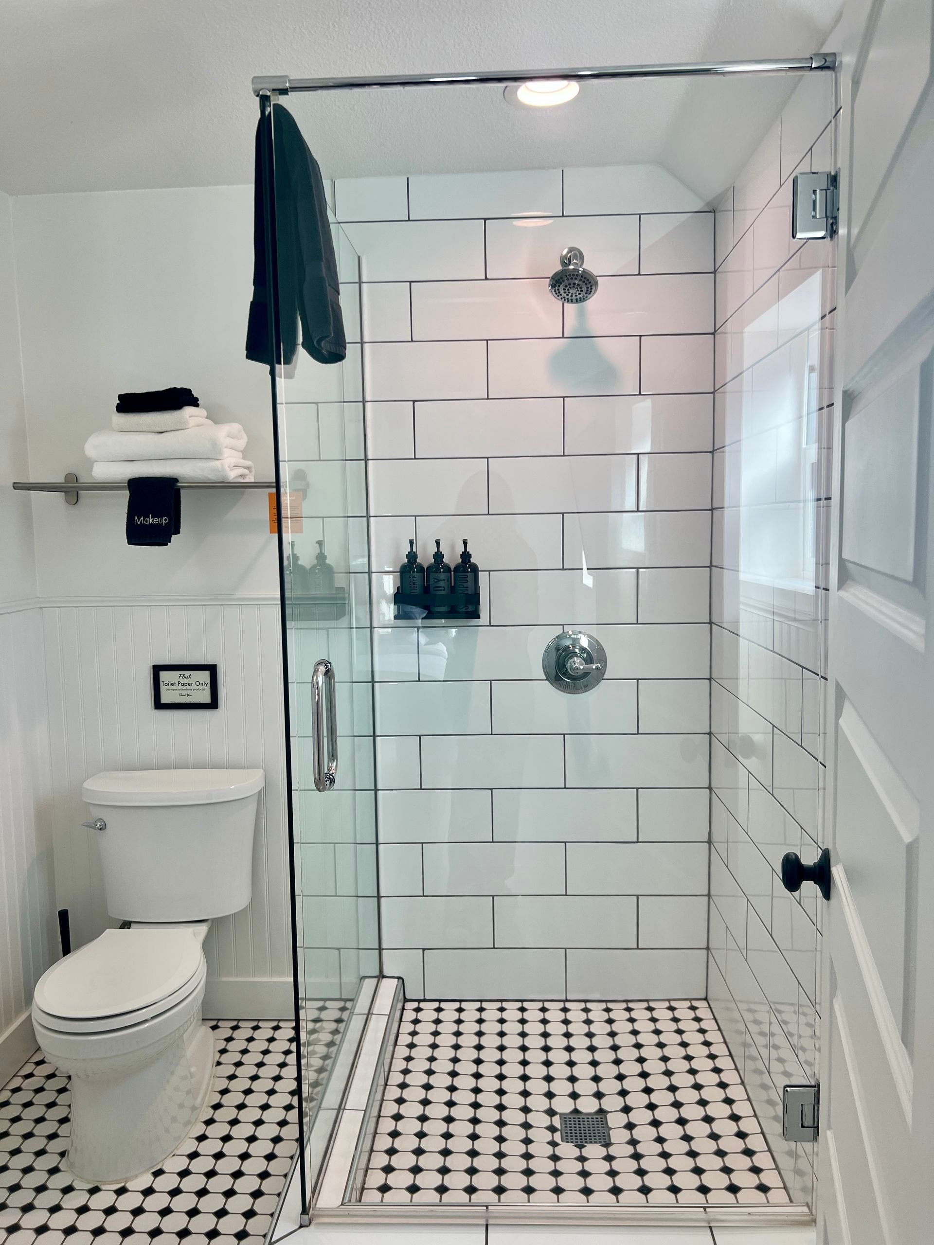 Small, modern bathroom with a glass shower, white tiles, and a black and white tiled floor.