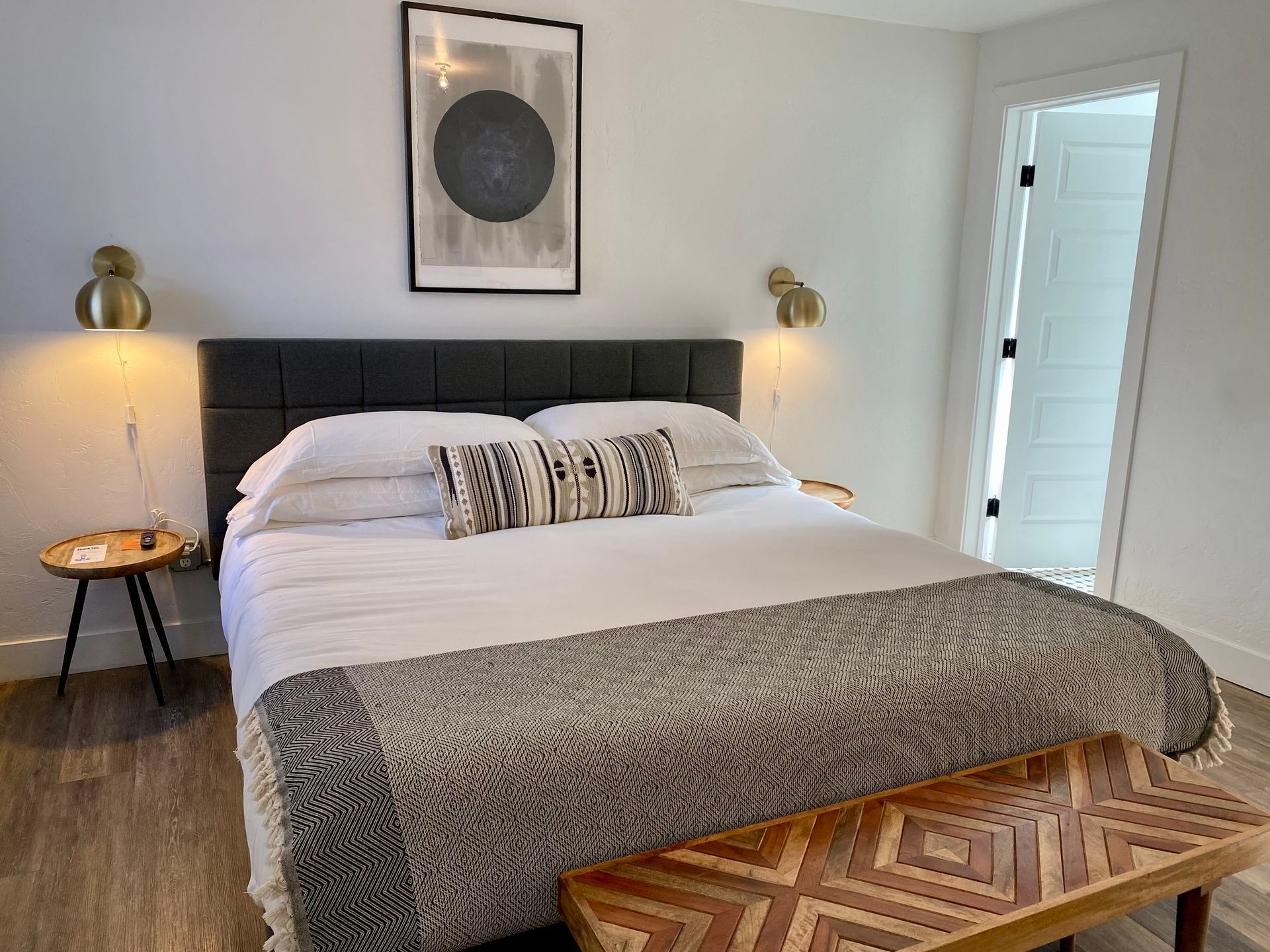 Bedroom with a bed, small tables, sconces, and artwork. A patterned wooden bench is at the foot of the bed.