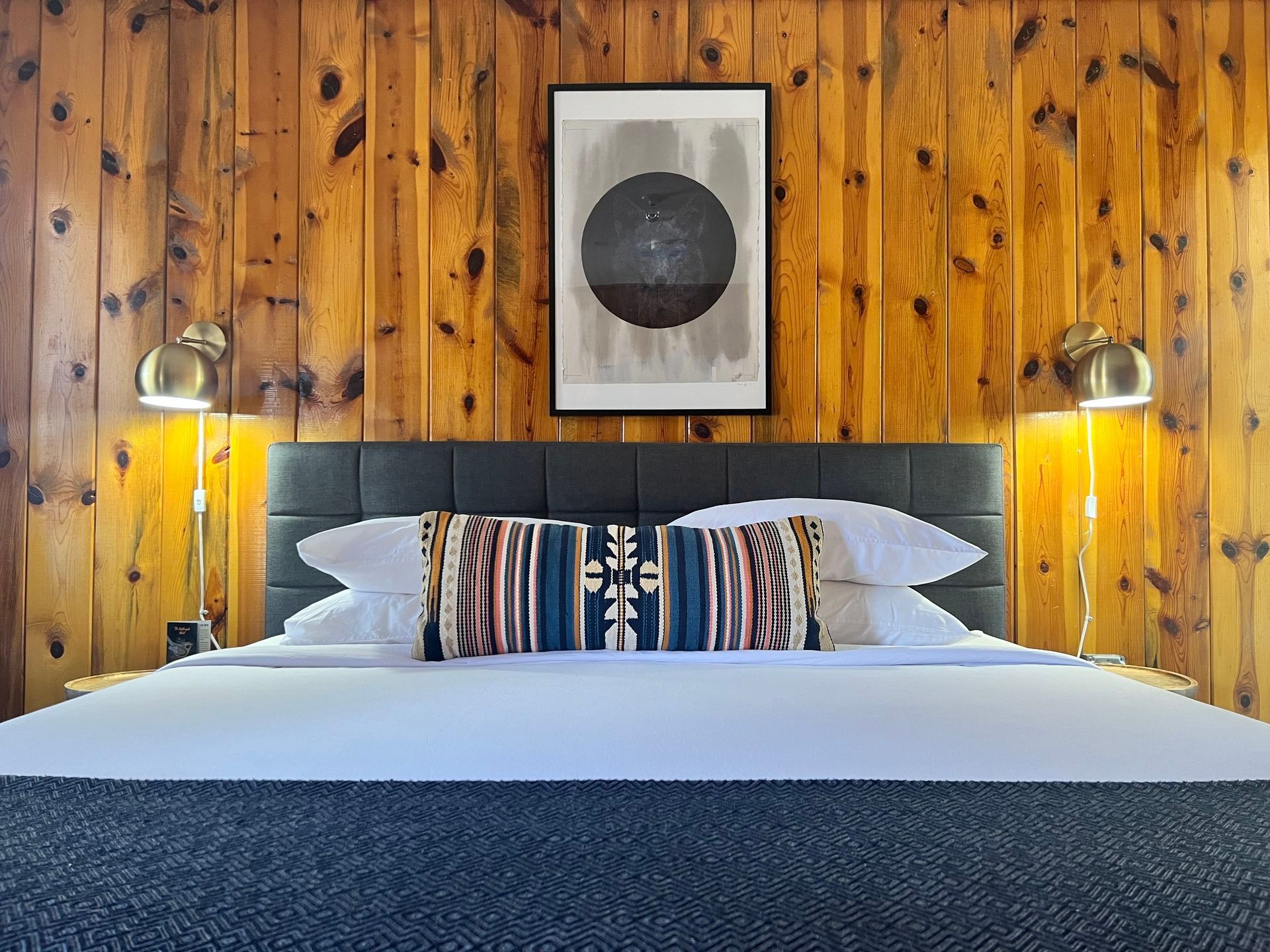 Bedroom with a wooden wall, bed with pillows, and a framed abstract print.