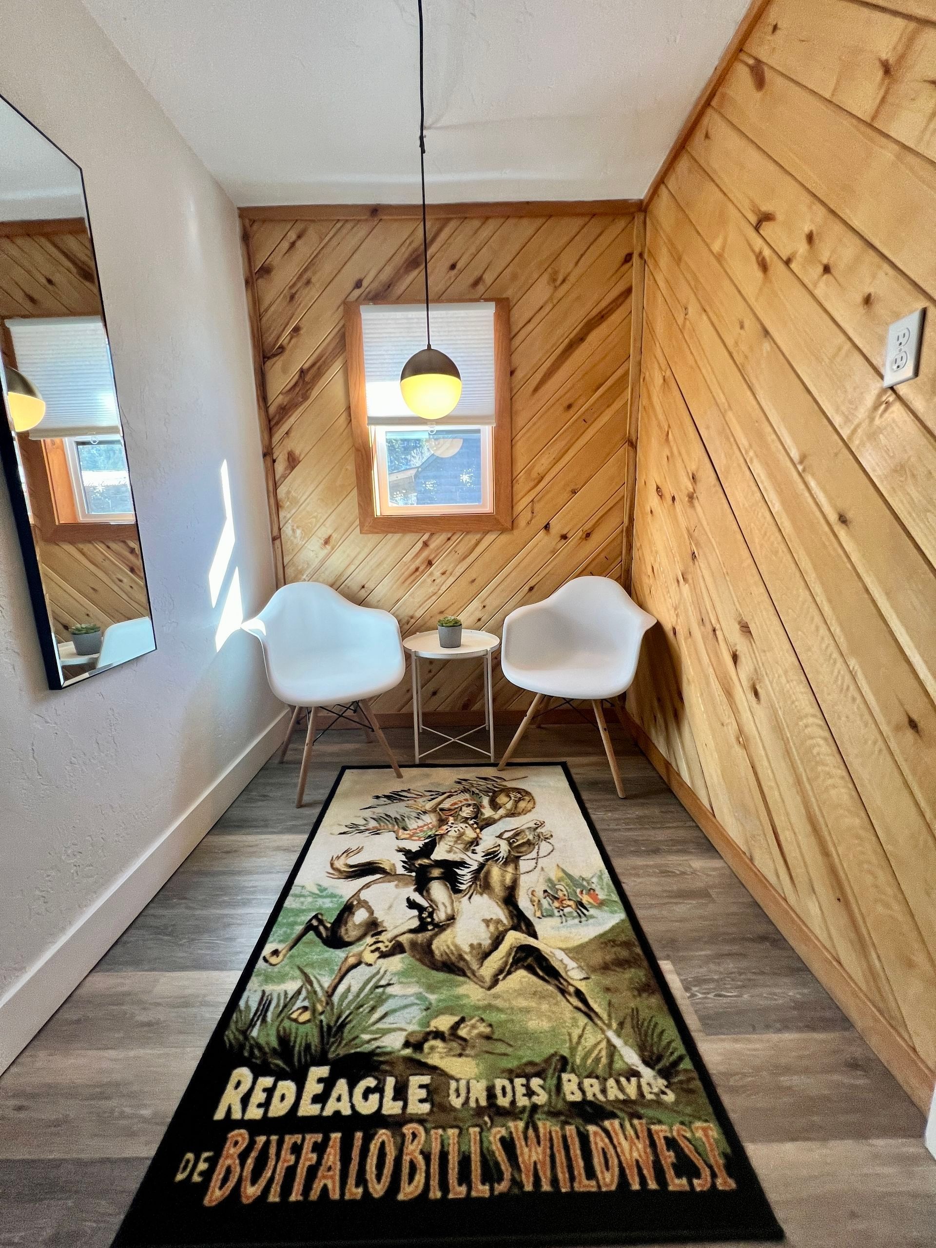 A cozy nook with wooden walls, two white chairs, a vintage rug, and a small table.