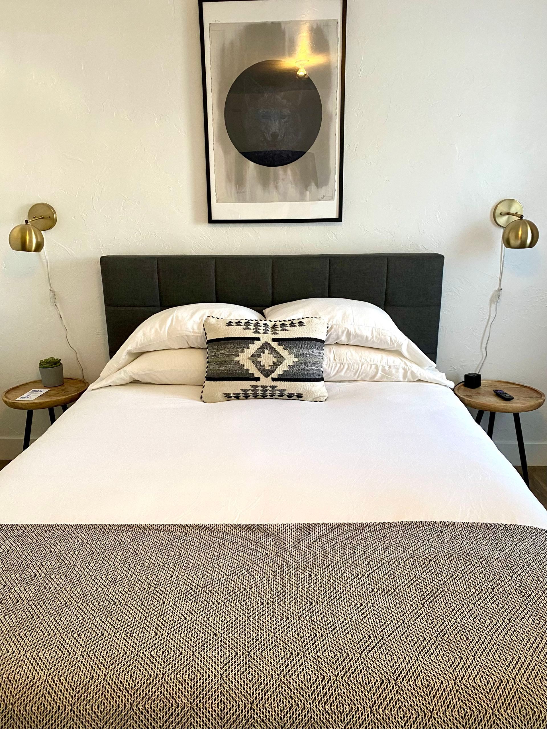 Bedroom with a bed, artwork, lamps, and nightstands. White bedding and a patterned bed runner.
