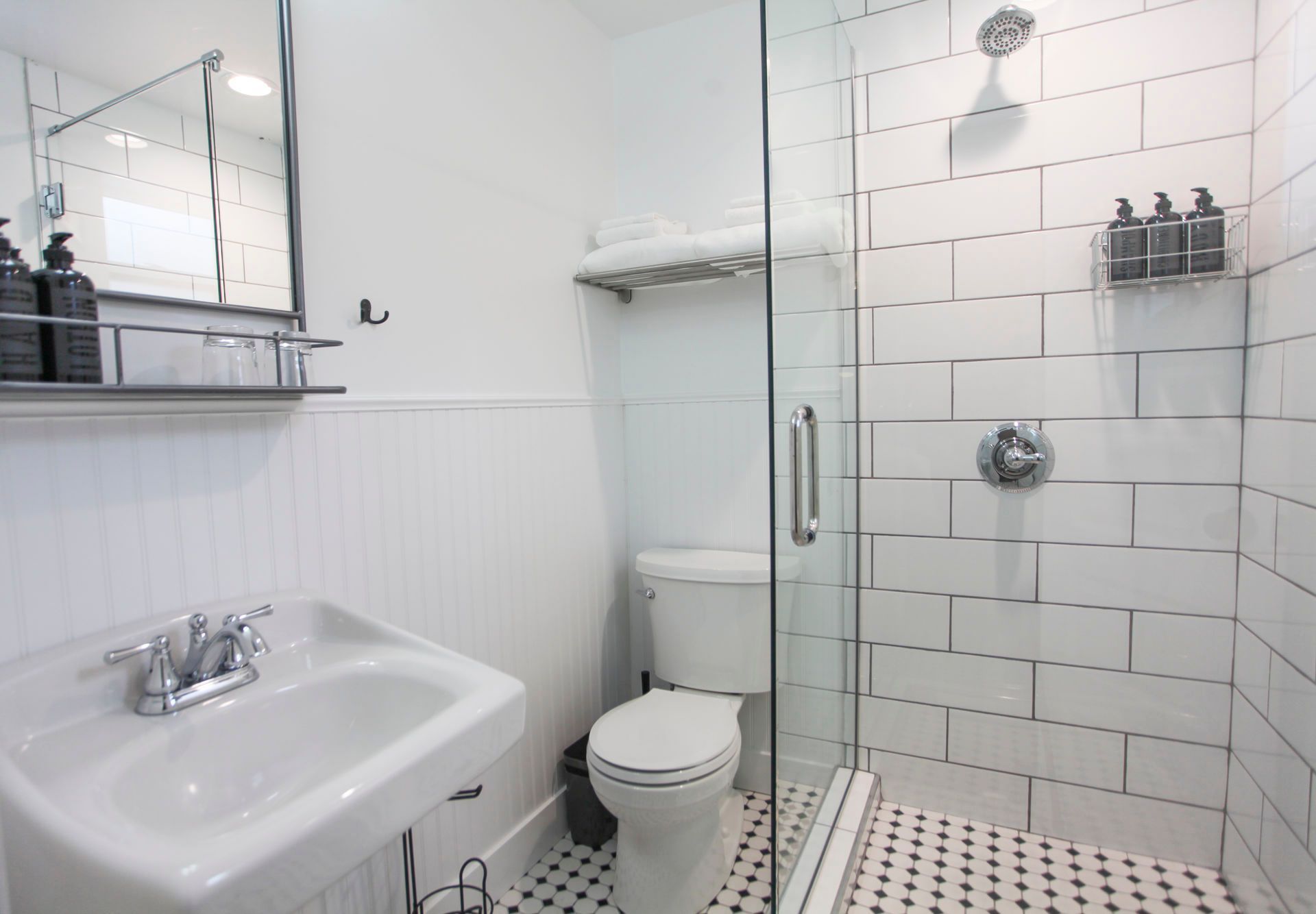White bathroom with a shower, sink, and toilet. Black and white tile.
