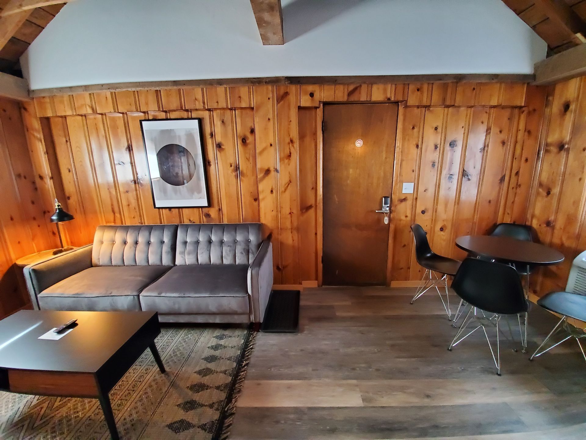 Living room with wood paneling, gray sofa, modern furniture, and door.