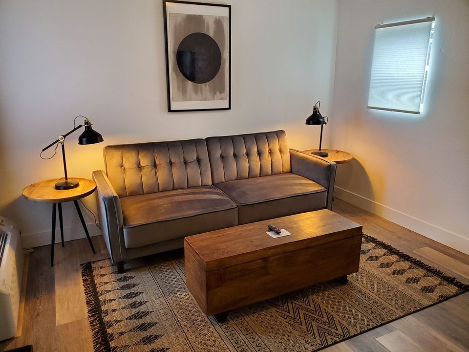 A living room with a gray couch, wooden coffee table, lamps, and art on the wall.