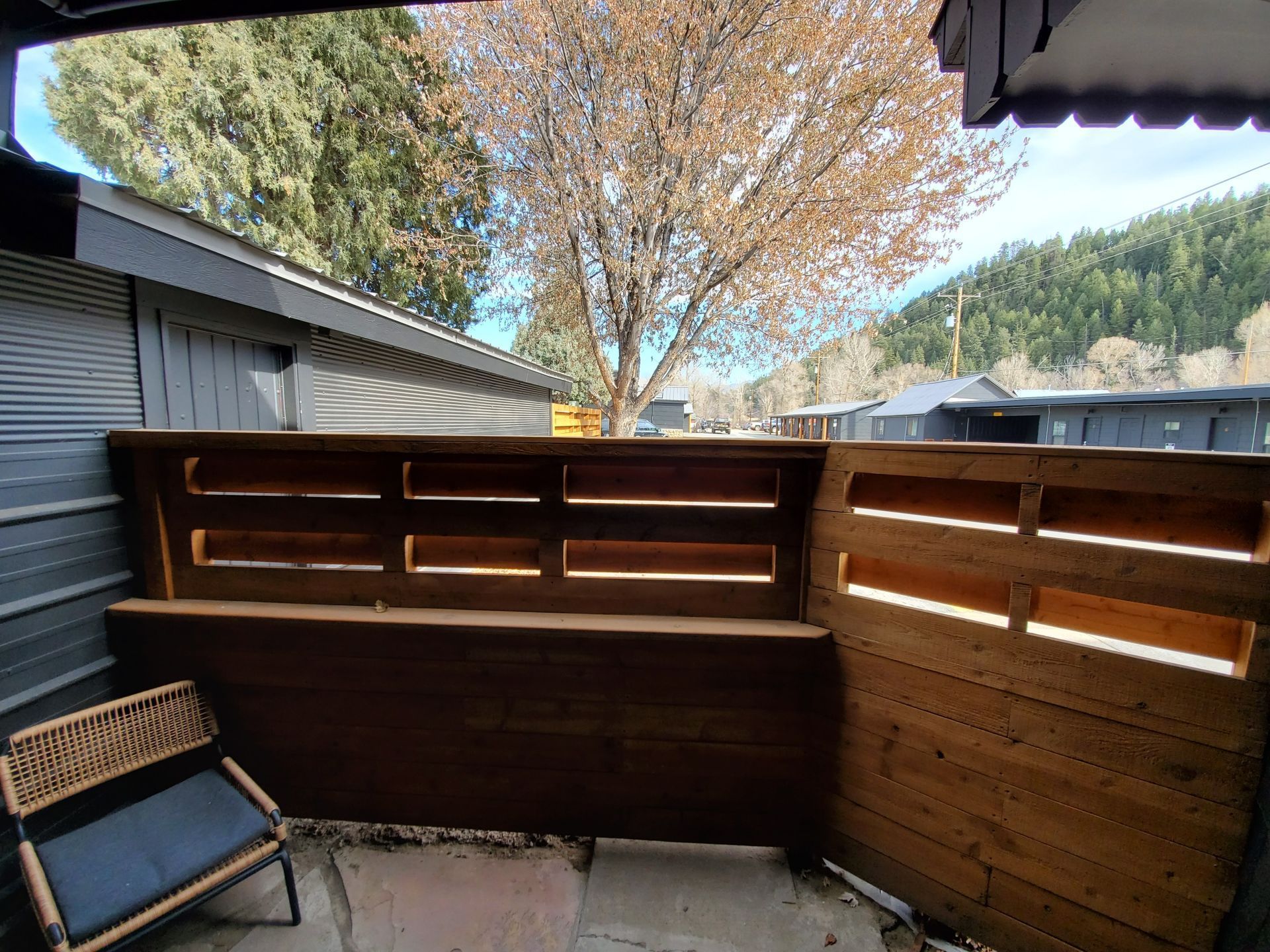 Patio with wooden fence, chair, and view of trees and buildings.