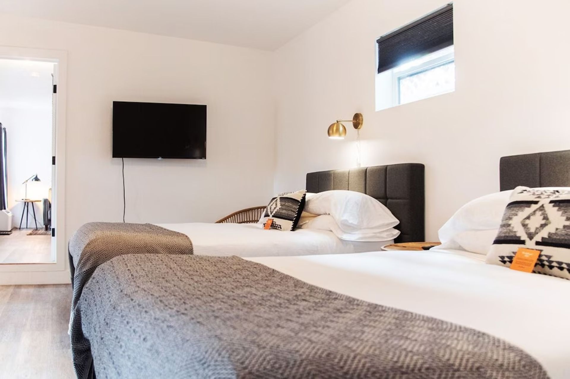 A modern hotel room with two beds, a television, and an open doorway.