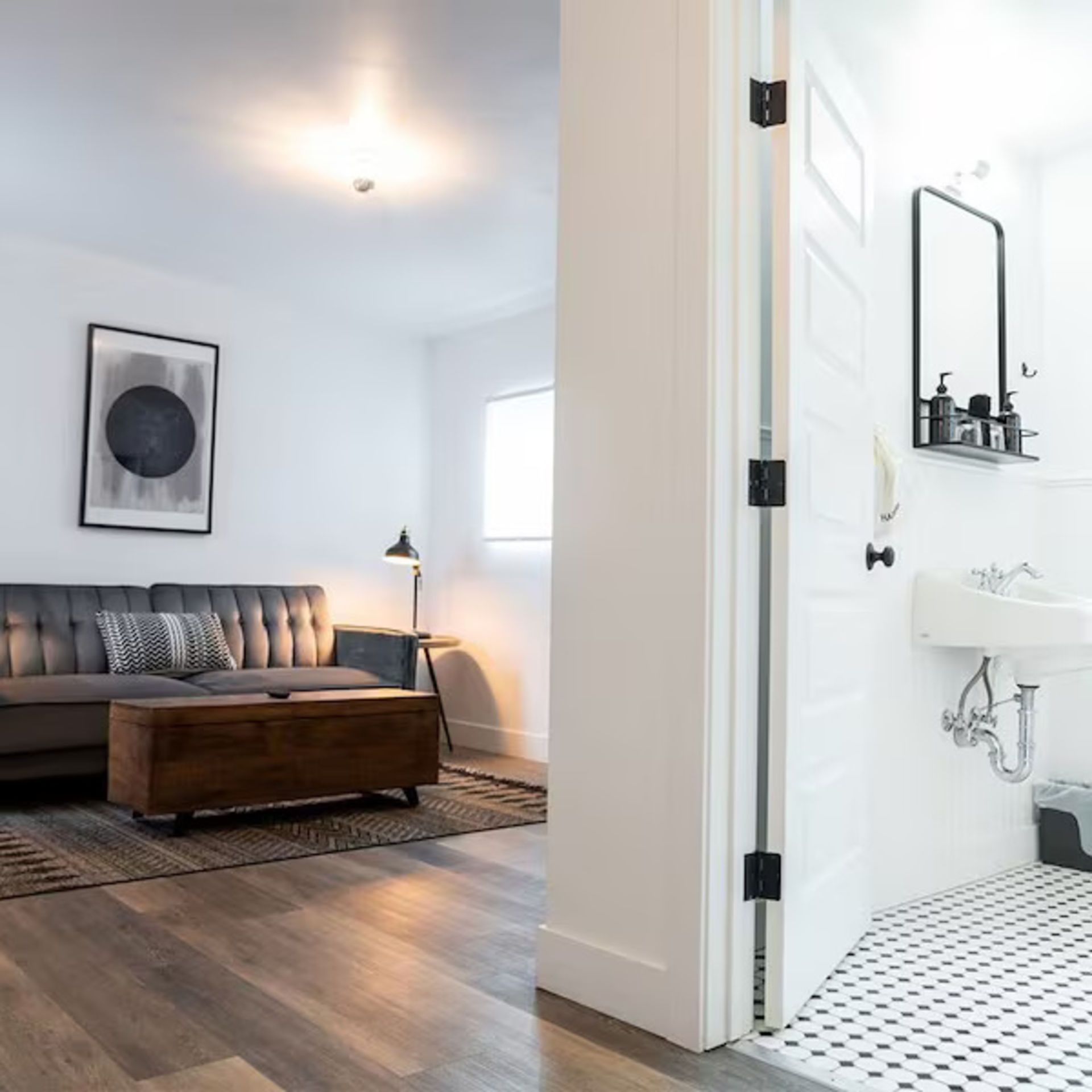 Living room with a sofa, a bathroom with a sink and a black and white tiled floor.