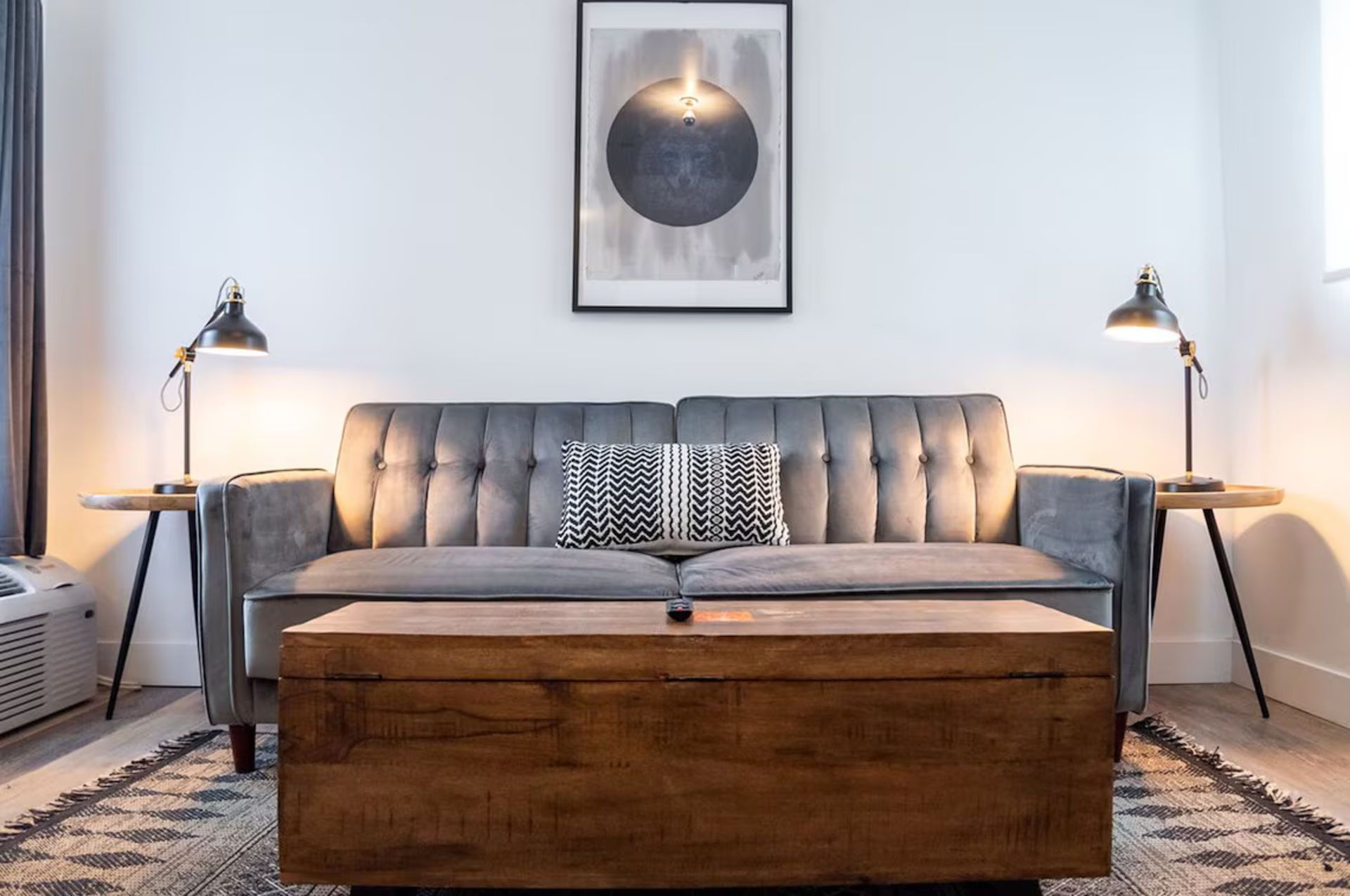 Cozy living room with gray couch, wooden coffee table, side tables, lamps, and abstract art.