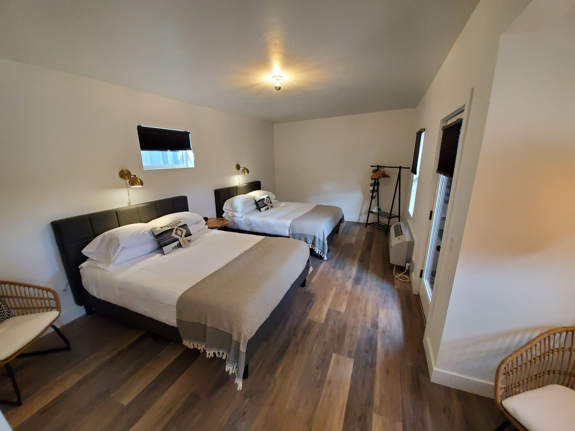 A hotel room with two queen beds, two chairs, and a wooden floor.