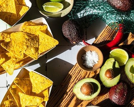 Tortilla chips, avocados, limes, salt, and chili peppers on a wooden board, ready for guacamole.
