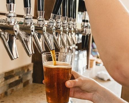 Person pouring beer from a tap into a pint glass. Pub setting, brown beer.