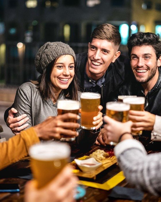 Friends toasting beers at a pub at night; they are smiling and looking at each other.