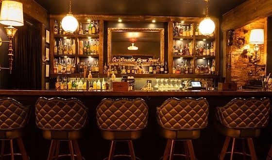 Bar with tufted stools, well-stocked shelves, and soft lighting.