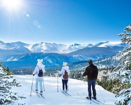 Three skiers on a snowy mountain, enjoying the view of a sunny, blue-sky landscape.