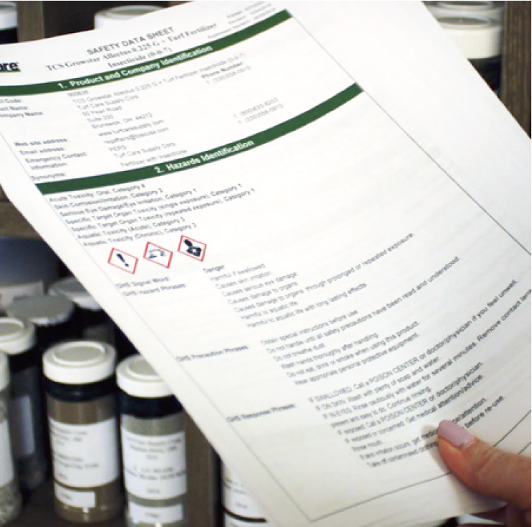 A person is holding a safety data sheet in front of bottles