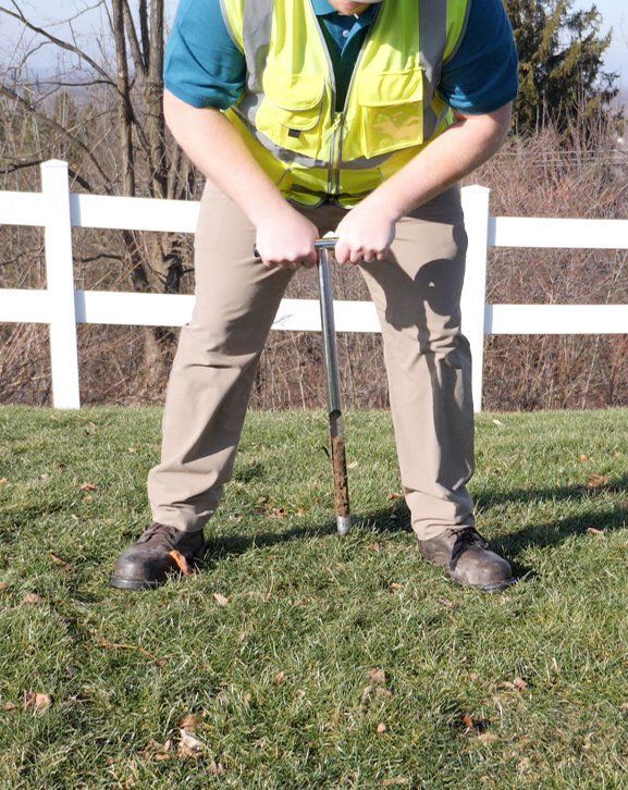 A man in a yellow vest is collecting soil samples