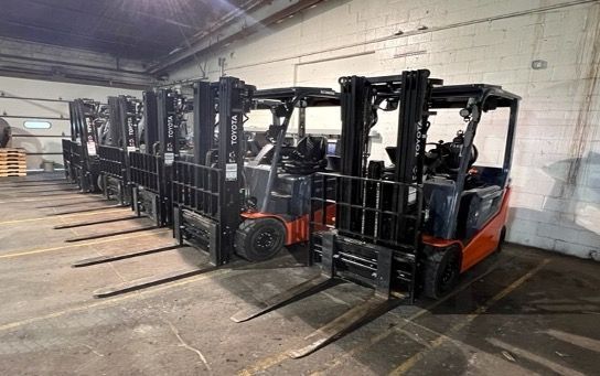 A row of forklifts are parked in a warehouse.