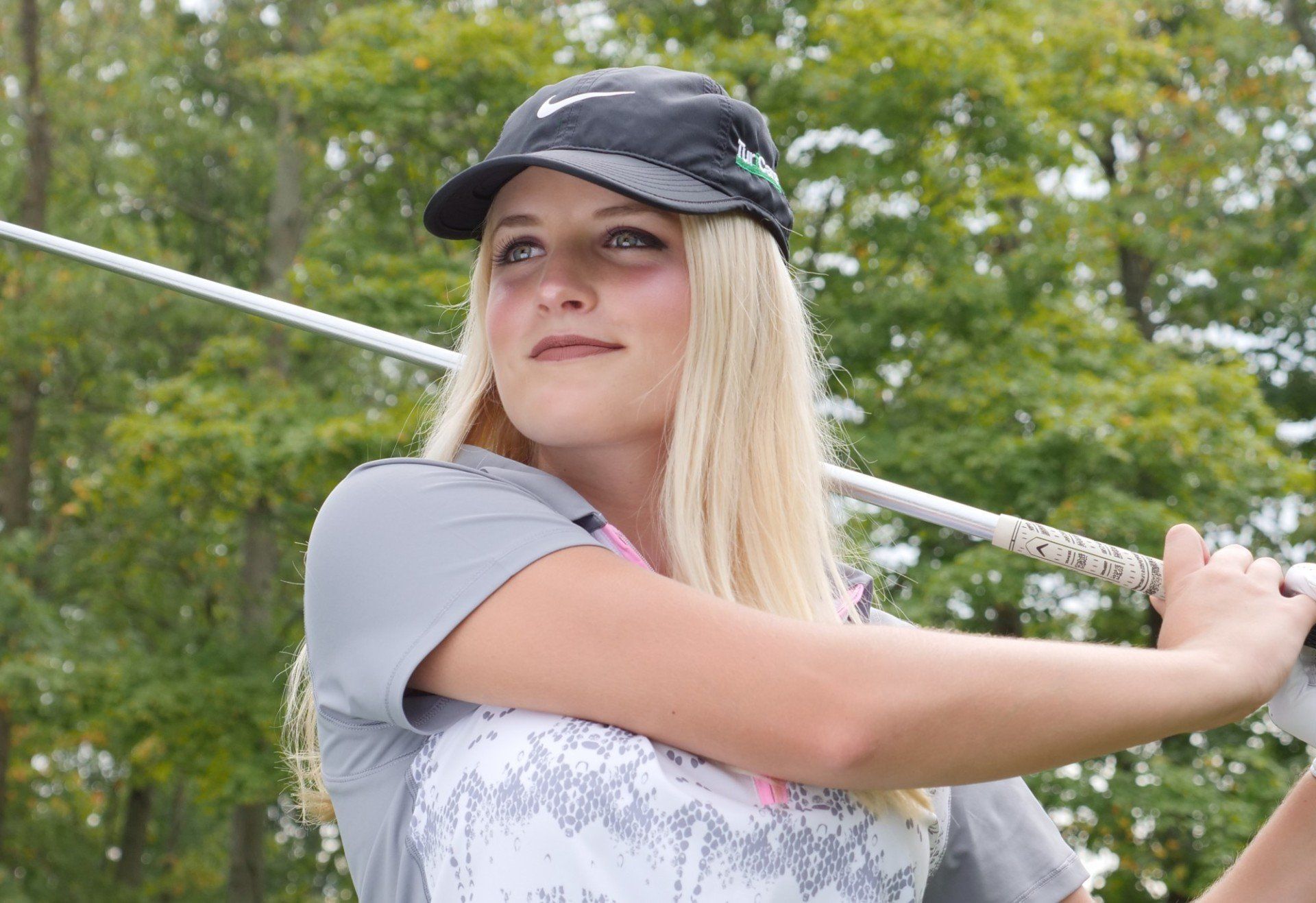 Nicole Gerome is swinging a golf club on a golf course.