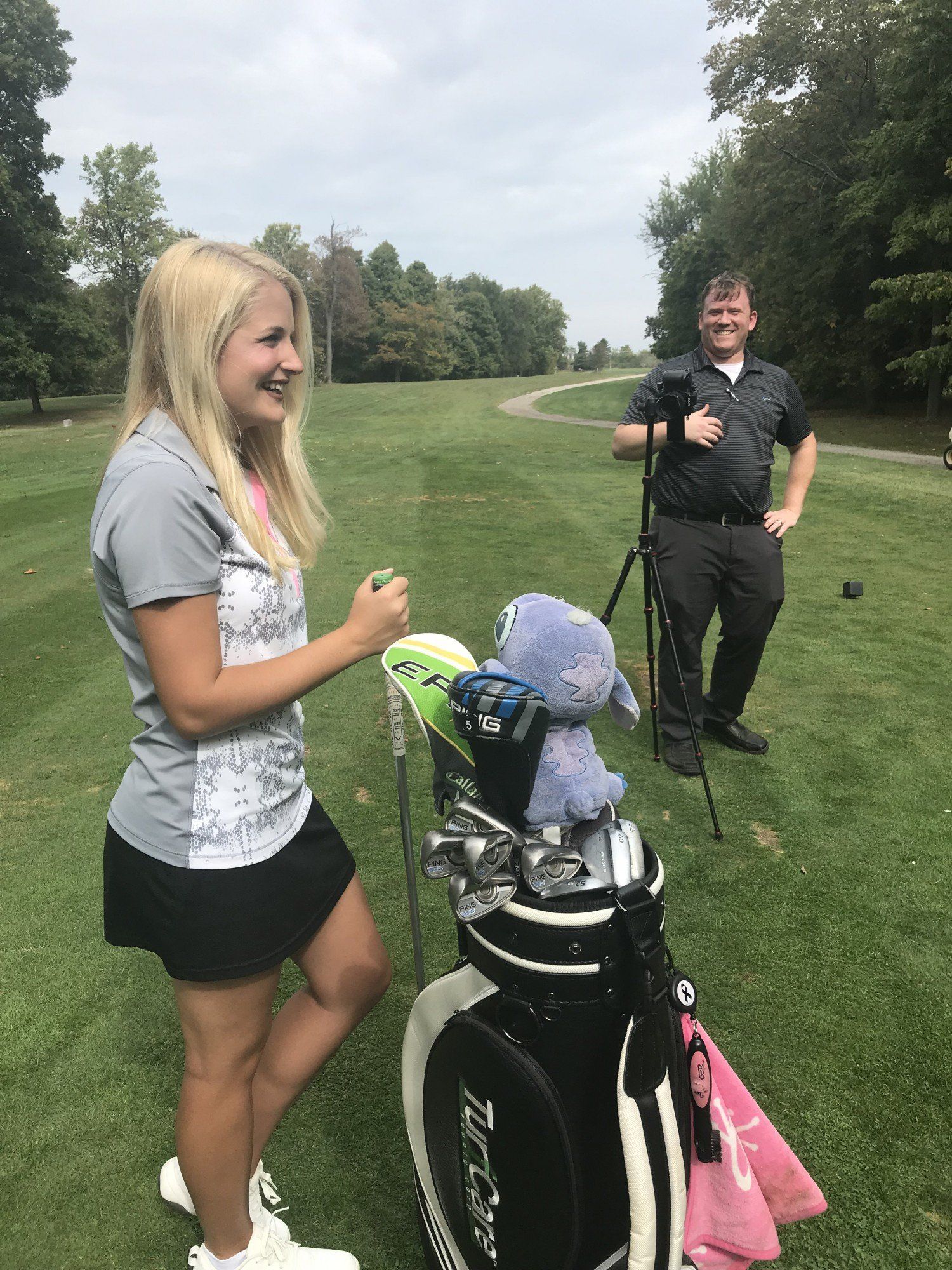 Nicole Gerome is standing next to a golf bag on a golf course.