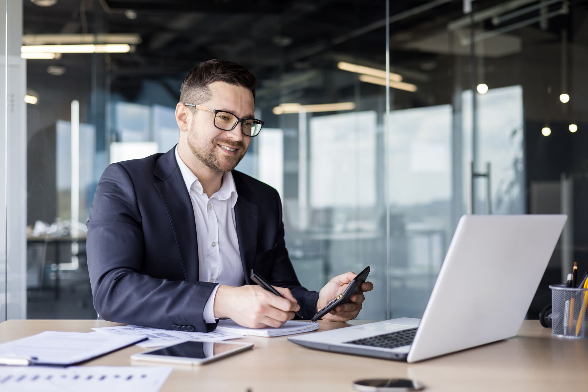 A man is sitting at a desk with a laptop and a cell phone.