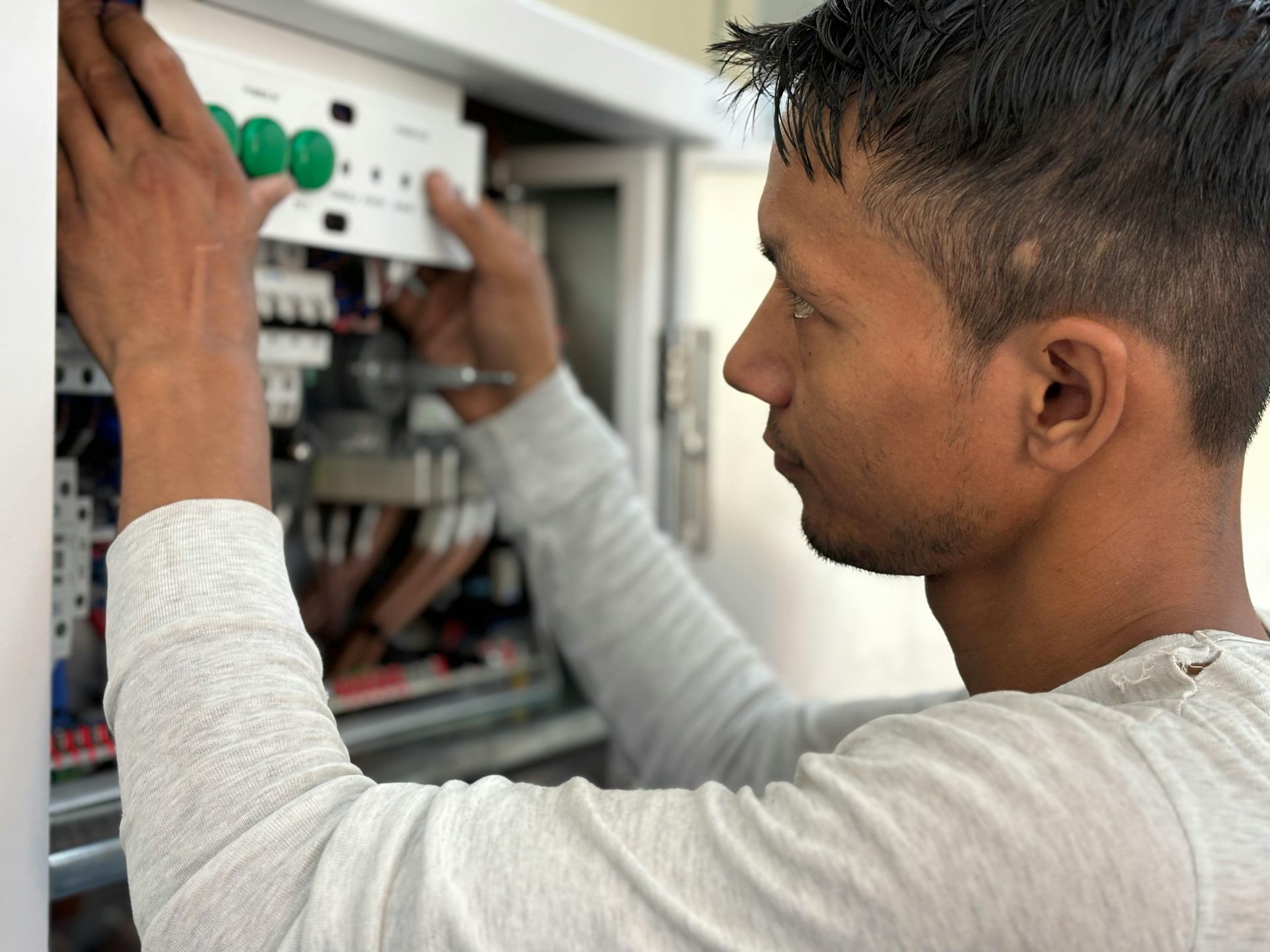Electrician working on electrical panel, wearing gray long-sleeve shirt.