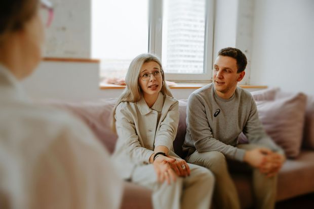 A man and a woman are sitting on a couch talking to a woman.