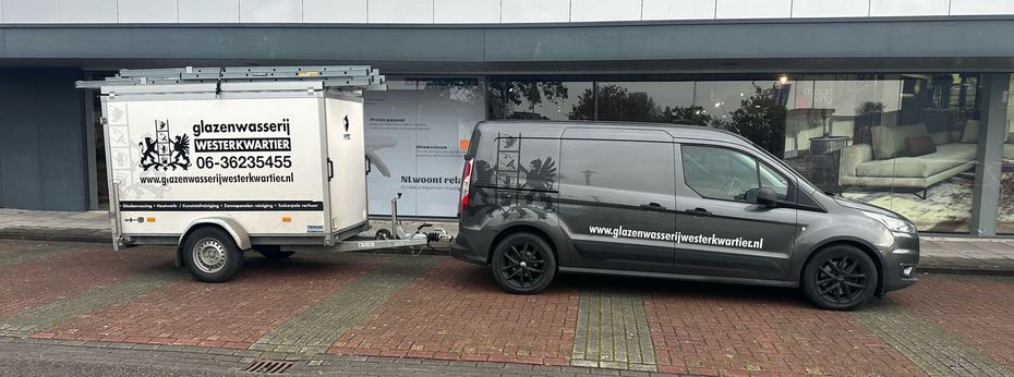 Een busje met een aanhanger staat voor een gebouw geparkeerd.