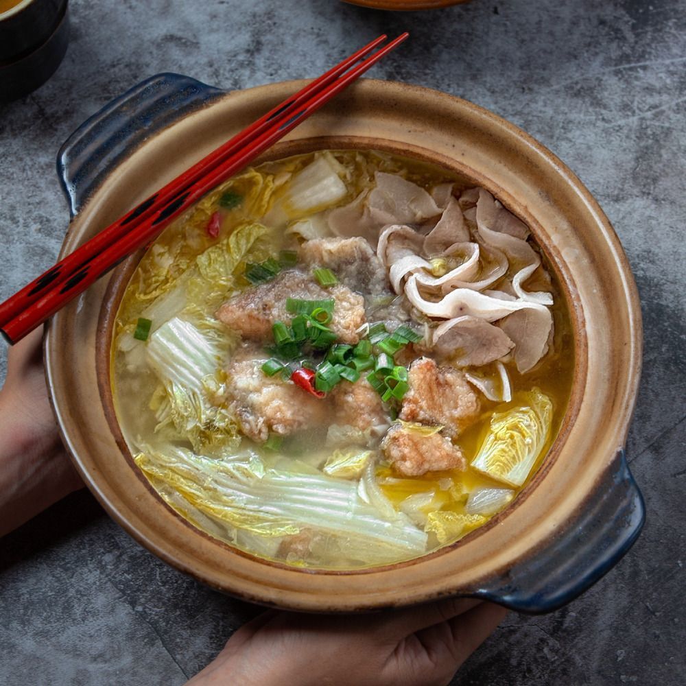 雙手捧著一口盛有魚、豬肉和蔬菜的中國湯的陶罐,上面放著筷子。