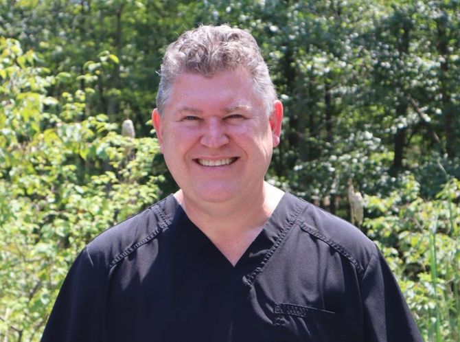 Dr. Waldron in a black scrub top is smiling in front of trees.