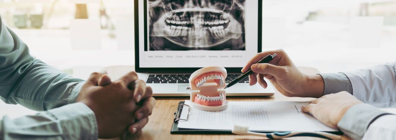 A man and a woman are sitting at a table with a laptop and a model of teeth.