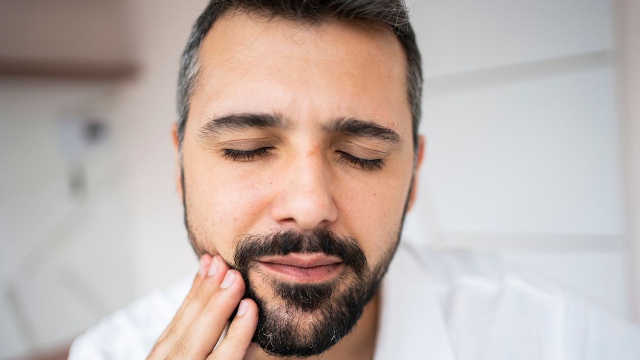 A man with a beard is holding his face in pain.