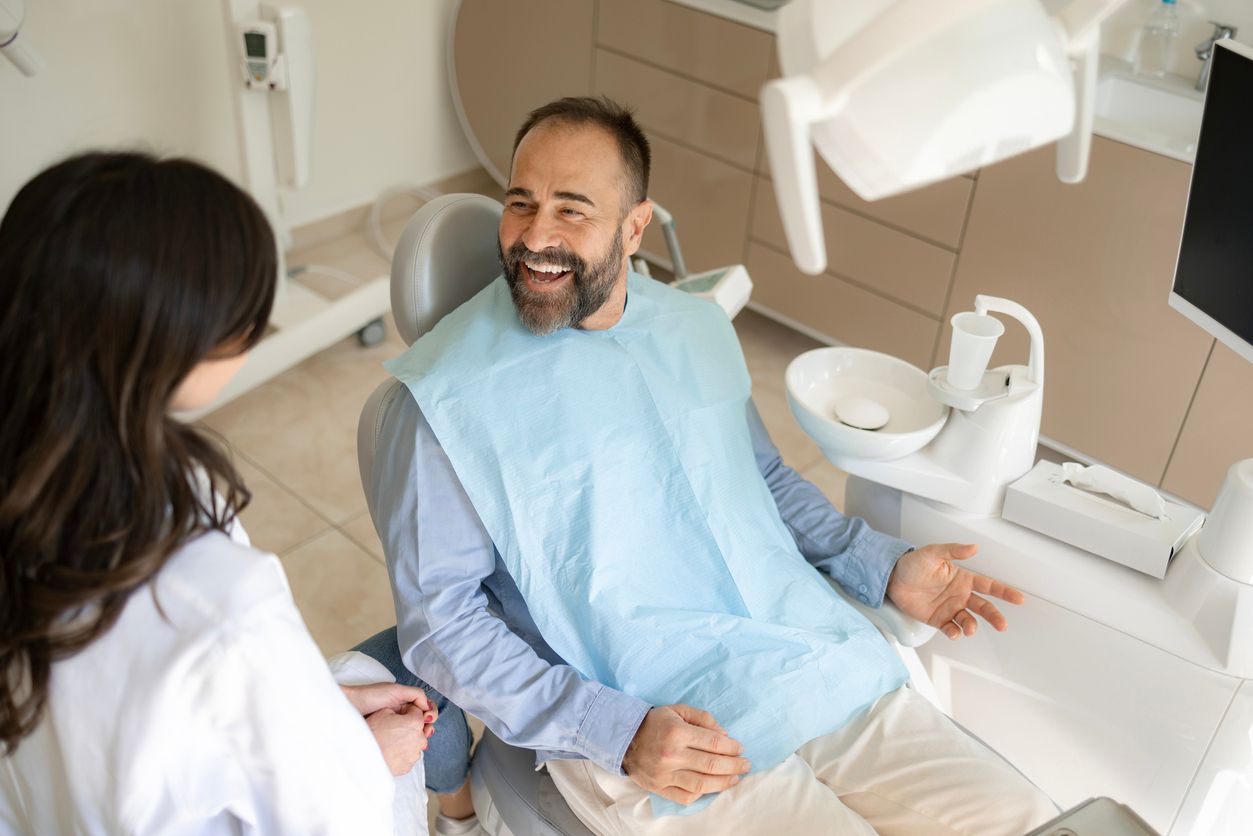 A man is sitting in a dental chair talking to a dentist.