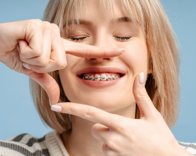 A woman with braces on her teeth is making a frame with her fingers.