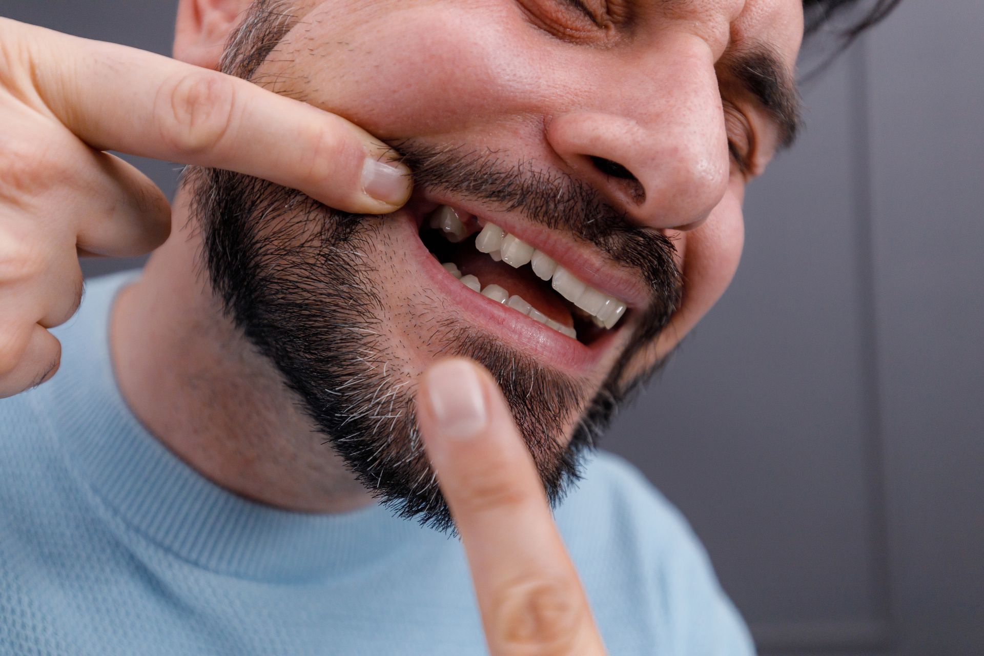 Man pointing at missing tooth, grimacing with pain, close-up shot.