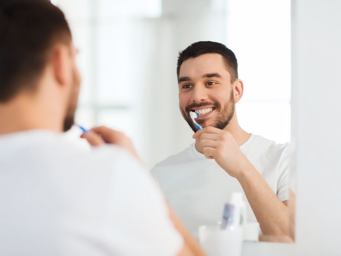 A man is brushing his teeth in front of a mirror.