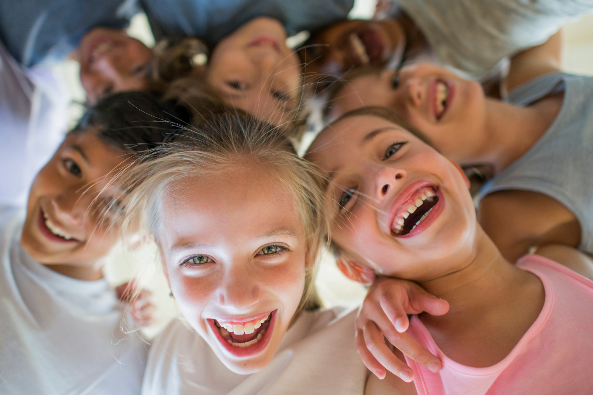 Children smiling and looking down, forming a circle. They are in a well-lit space.