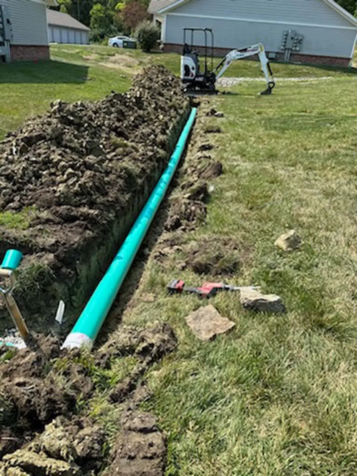 A green pipe is being installed in a yard next to a house.