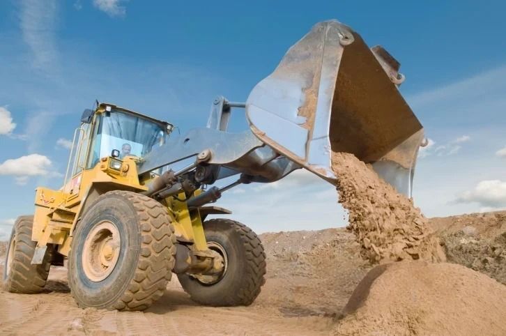 A bulldozer is pouring dirt into a pile of dirt.