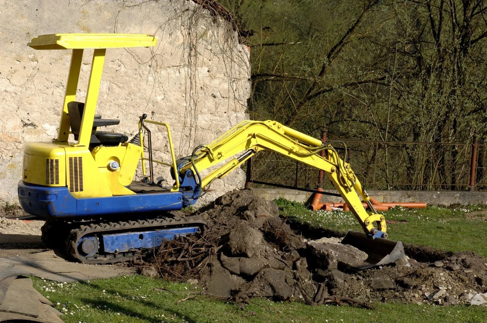 A yellow and blue excavator is digging a hole in the dirt.