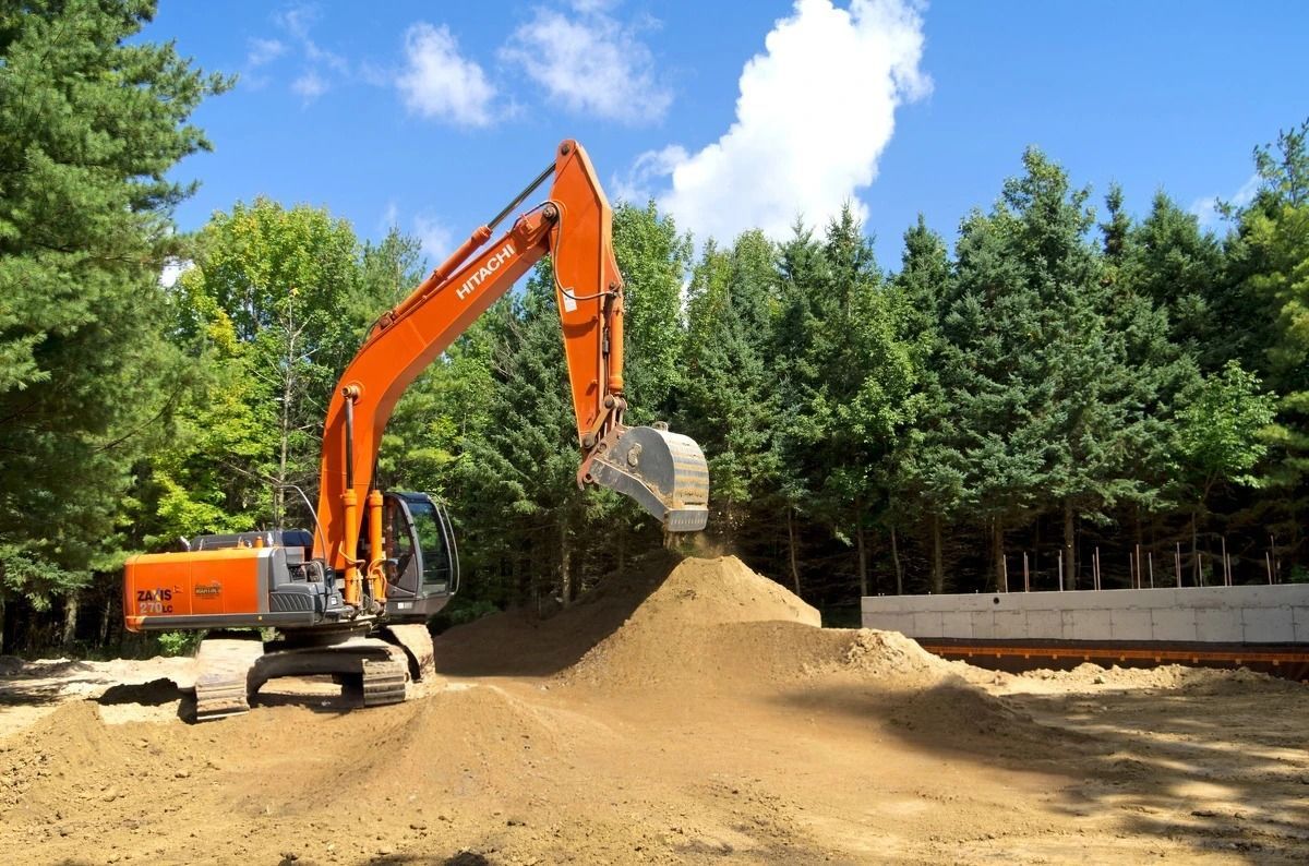 A large orange excavator is loading dirt into a pile.