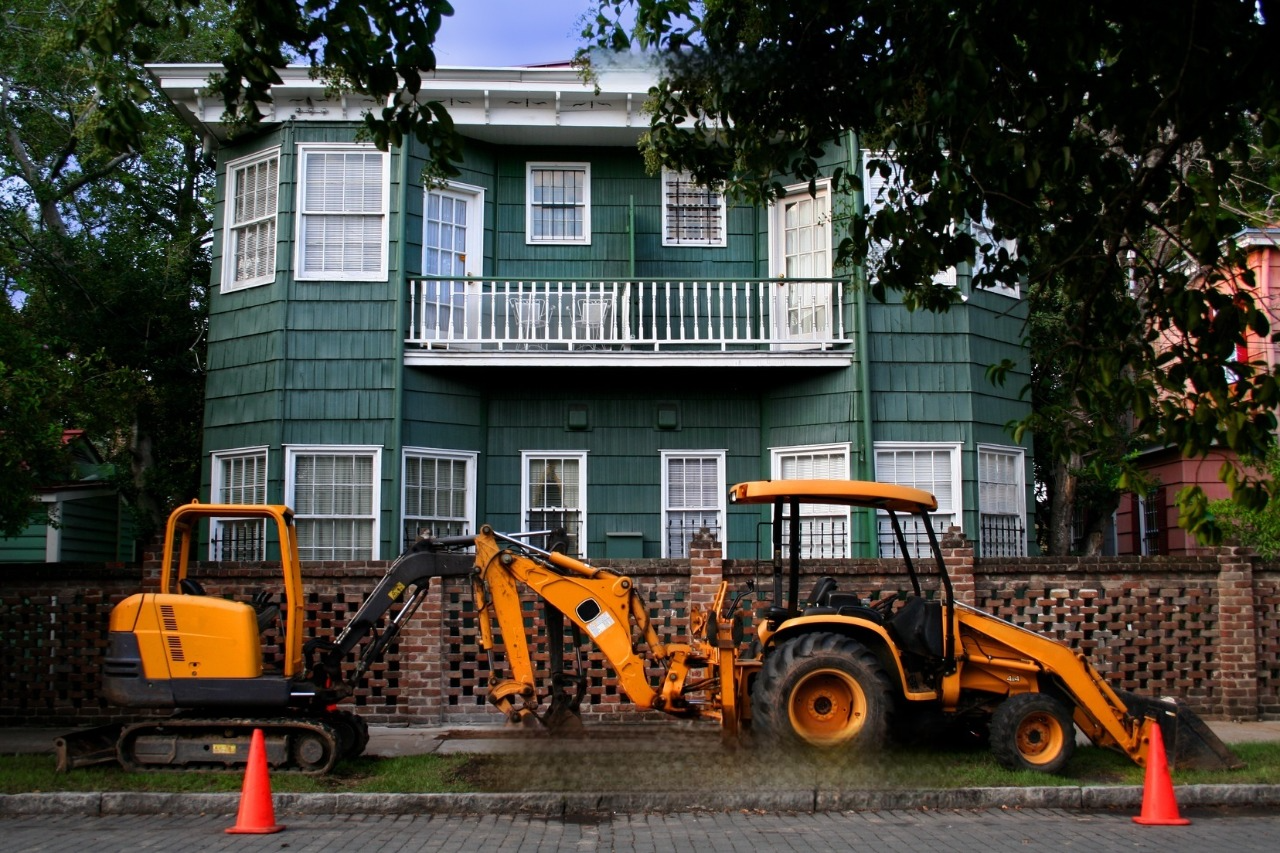 A yellow excavator is parked in front of a green building.