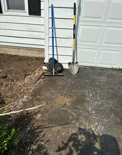 A shovel and rake are sitting on the sidewalk in front of a garage door.