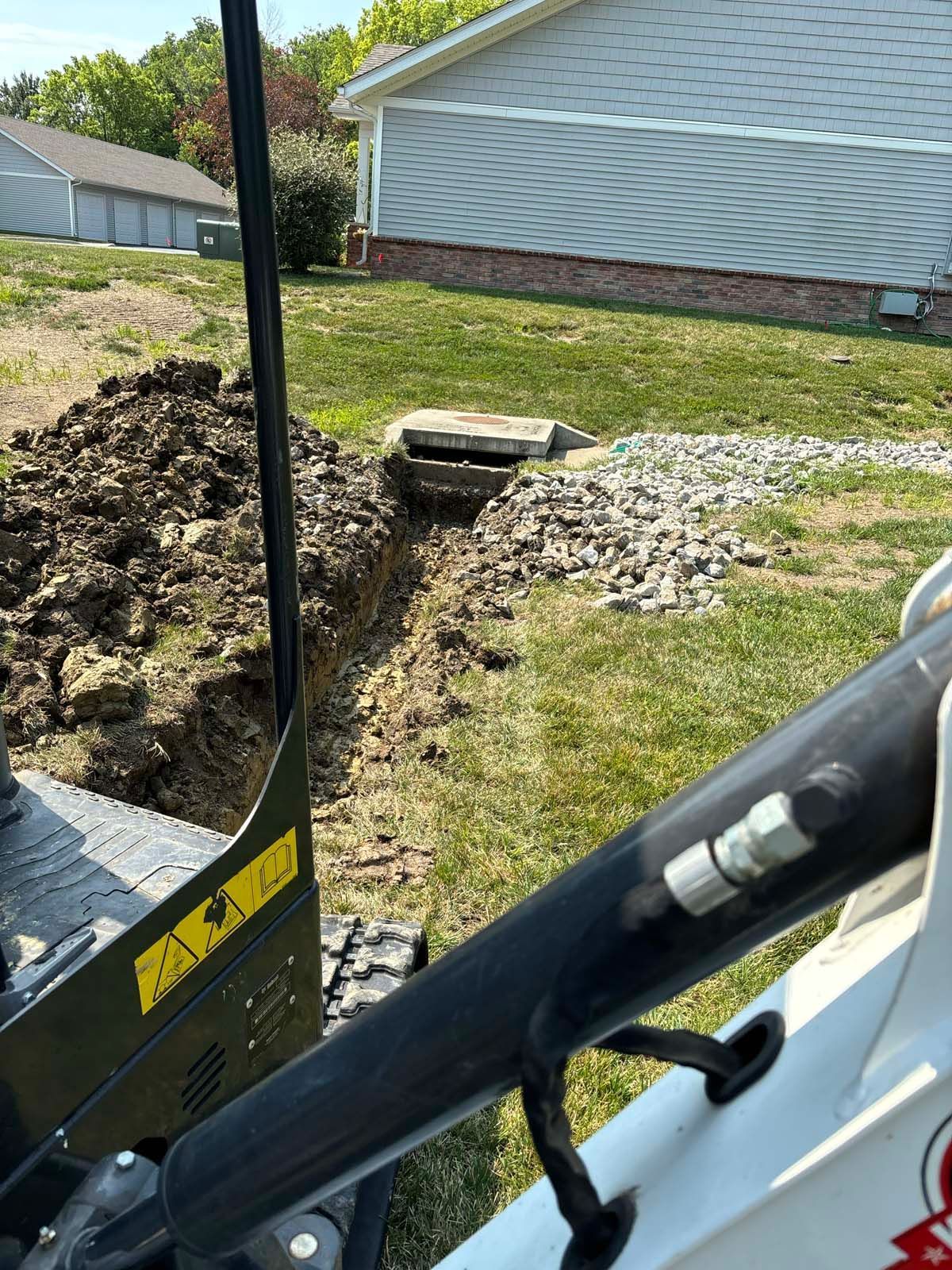 A bulldozer is digging a hole in the grass in front of a house.