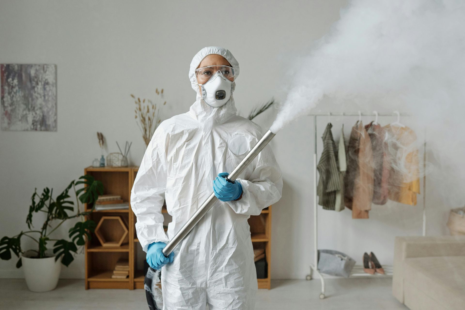 A man in a protective suit is spraying a room with a sprayer.