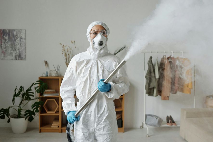 A man in a protective suit is spraying a room with a sprayer.