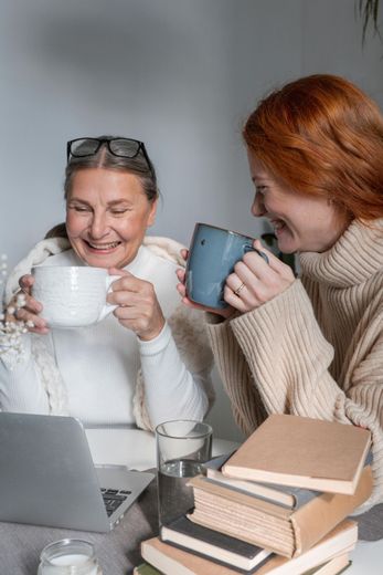Two women are sitting at a table drinking coffee and looking at a laptop.