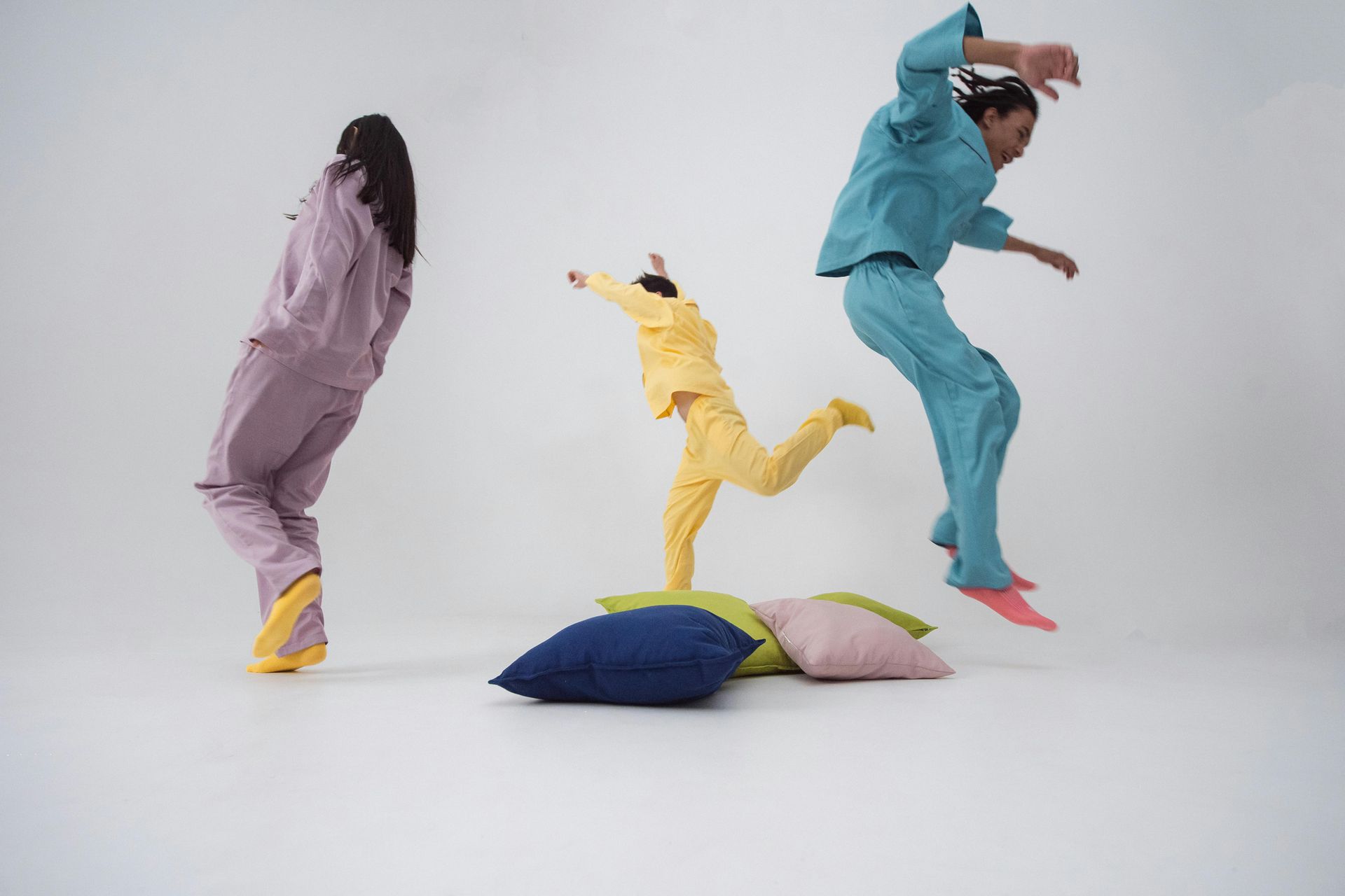 Three people in pajamas are jumping in the air over pillows.
